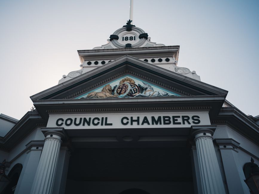 Close-up view of the front facade of a municipal building with the sign 'Council Chambers' displayed above the entrance, featuring classical architectural elements such as white columns, decorative mouldings, and a triangular pediment with a crest, lion figures, and the year '1881,' with part of the sky visible in the background. This exterior shot is related to the process of house removals and local authority permits, often relevant in planning for home relocation or furniture transport in Snaresbrook, as managed by Man with Van Snaresbrook, a specialist in removals services.