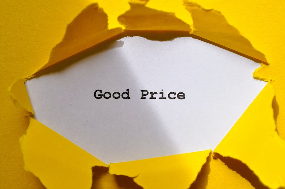 A close-up photograph of a piece of yellow paper with a large tear in the center, revealing a white surface underneath that displays the words 'Good Price' in black typewriter-style font. The torn edges of the yellow paper are jagged and curled outward, showing the thickness and texture of the material. The background is plain and matching the yellow color of the torn paper, emphasizing the focus on the message. The image subtly relates to affordable pricing in house removals and moving services, highlighting transparent and cost-effective home relocation options through [COMPANY_NAME] and its service offerings.